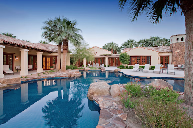 Spanish style house with a large swimming pool and palm trees in the backyard.