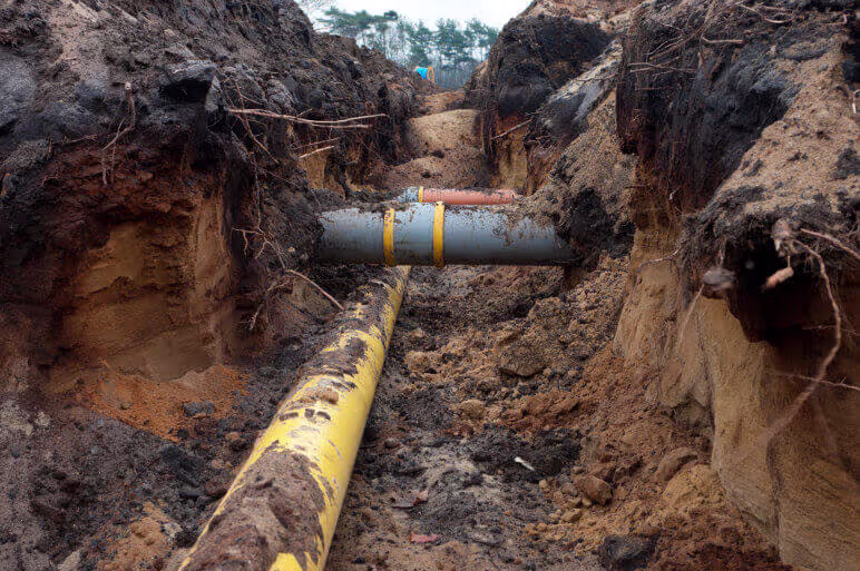 Yellow and gray underground utility lines visible in a trench dug in the dirt.